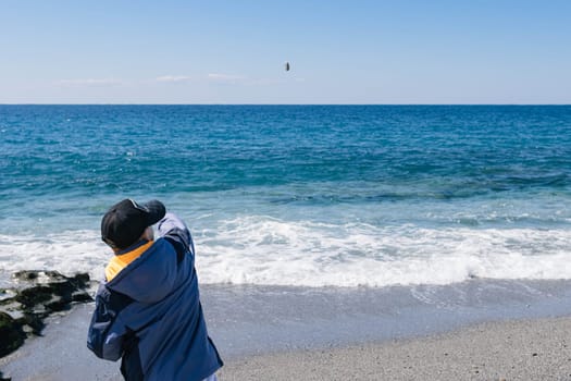 a child stands on the seashore and throws pebbles into the water in the sea.View from behind.Beautiful background. High quality photo