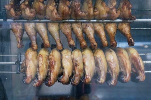 chicken legs are fried in a shop window for sale to hungry people, smoke a grill. High quality photo