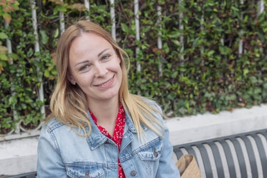 a girl of European appearance with blond hair in a denim jacket sits in a park and thinks daydreams holding her hand to her head close-up portrait a girl . High quality photo