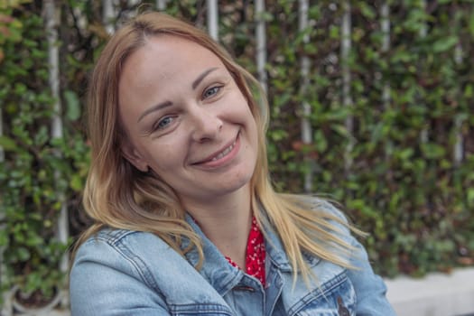 a girl of European appearance with blond hair in a denim jacket sits in a park and thinks daydreams holding her hand to her head close-up portrait a girl . High quality photo