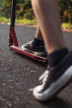 boy on a scooter legs close-up sneakers black and white red scooter.blurred background. High quality photo