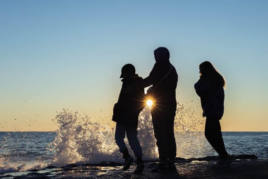 on the seashore, a family of mother, daughter and son look at the waves, there is a place for an inscription people stand with their backs at sunset. High quality photo