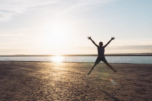 a cheerful child jumps up against the background of the sky, ocean and sand on the beach at sunset. Silhouette of a cheerful boy at sunset. Beautiful landscape,High quality photo