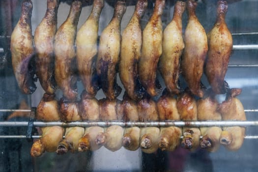 chicken legs are fried in a shop window for sale to hungry people, smoke a grill. High quality photo