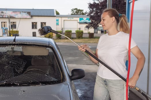 a girl with blond hair in a white T-shirt and jeans washes a car at a self-service car wash. High quality photo