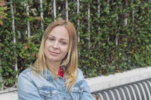 a girl of European appearance with blond hair in a denim jacket sits in a park and thinks daydreams close-up, a portrait on the right there is a place for an inscription.High quality photo