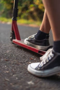 boy on a scooter legs close-up sneakers black and white red scooter.blurred background. High quality photo