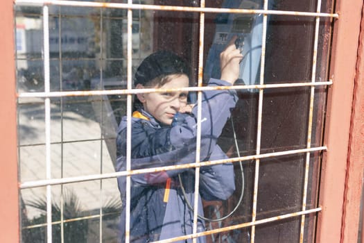 a boy of European appearance in a telephone booth is talking on the phone. Front view through the glass close-up Old telephone booth. High quality photo