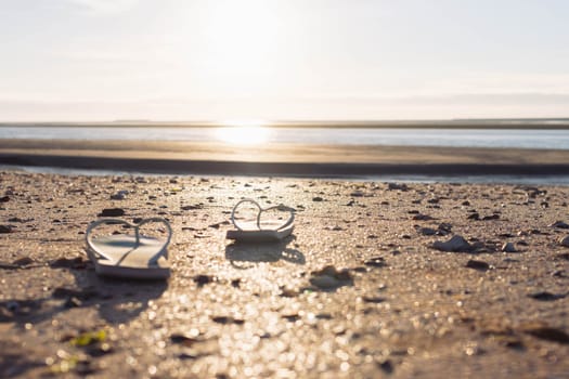 on the beach on the sand, a pair of beach slippers stands close-up and the background is blurred at sunset, the photo is taken, a beautiful and creative beach background High quality photo