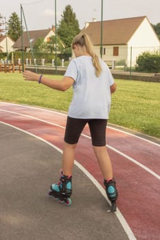 child of European appearance with blond hair tied in a ponytail learn to roller skate in the park dressed girl in a light T-shirt and black shorts. High quality photo