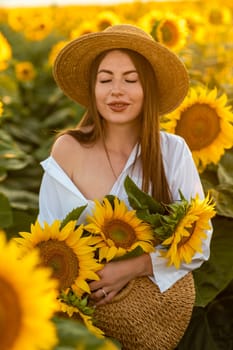 A girl in a hat on a beautiful field of sunflowers against the sky in the evening light of a summer sunset. Sunbeams through the flower field. Natural background