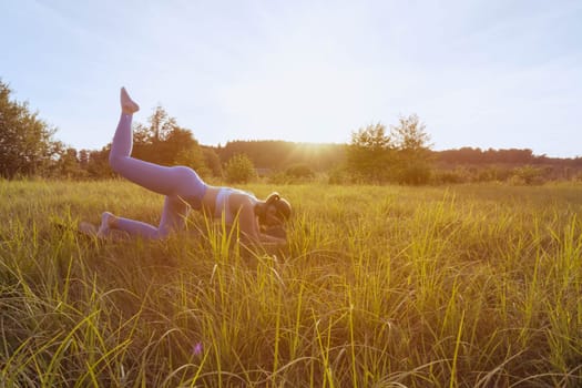 a girl is engaged in fitness outdoors on the grass, dressed in blue leggings and a white tank top.healthy lifestyle concept. High quality photo there is a place for an inscription