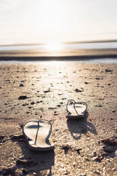 on the beach on the sand, a pair of beach slippers stands close-up and the background is blurred at sunset, the photo is taken, a beautiful and creative beach background High quality photo