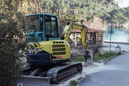 yellow excavator parked near the hill and the sea, the bulldozer works in summer. High quality photo