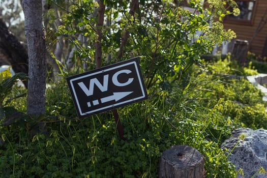 Direction to the toilet on the beach.WC - the inscription on the sign of the toilet hangs on a pole, sea, beach, green trees.Sunny summer day.Close-up view. High quality photo