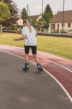 child of European appearance with blond hair tied in a ponytail learn to roller skate in the park dressed girl in a light T-shirt and black shorts. High quality photo