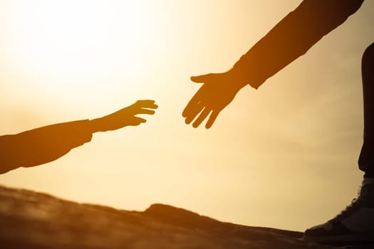 silhouette of hands on the mountain, a man gives a hand to a girl on a mountain, the concept of mutual assistance, motivation for success, place for an inscription. Helping hand. High quality photo