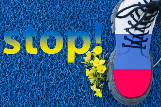 boot the flag of Russia steps on yellow flowers on a blue background.Flag of Ukraine.Left inscription stop.Aggressor,war in Ukraine. High quality photo