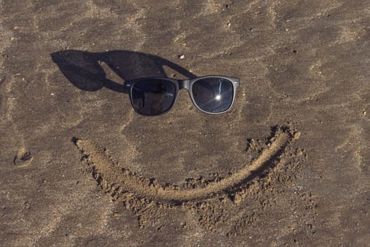 a smile is drawn on the sand on the beach and next to glasses instead of eyes lie a beautiful beach background with a place for an inscription. High quality photo