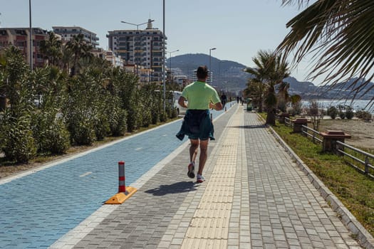 a man runs along the sidewalk around green palm trees and trees, on the sidewalk there is a marking of a bicycle path. The concept of a healthy lifestyle. High quality photo