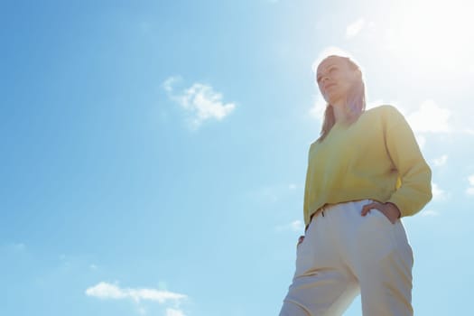 portrait of a girl against the blue sky, the girl is standing in a yellow jacket and white pants, there is a place for, a beautiful landscape with a girl, the concept of freedom. High quality photo