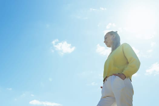 portrait of a girl against the blue sky, the girl is standing in a yellow sweater and white pants, there is a place for an inscription, a beautiful landscape with a girl. High quality photo