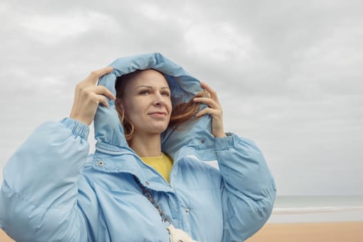 a girl of European appearance with blond hair stands on the seashore in a blue jacket, looks thoughtfully to the side. High quality photo