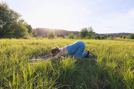 girl in a blue suit for fitness in the fresh air at sunset in the park goes in for sports, stands in the bar. There is green grass,the landscape is beautiful. The concept of sports. High quality photo