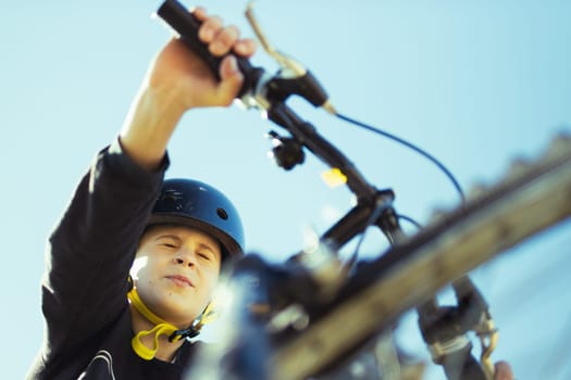 a teenager boy of European appearance with short blond hair in a T-shirt stands with a bicycle in the park.looks at the camera on the left there is a place for an inscription. High quality photo