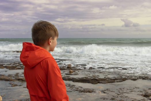 a boy of European appearance with blond hair in an orange windbreaker, standing on the embankment close-up, there is a place for an inscription. High quality photo