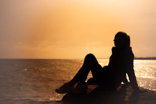 silhouette of a girl sitting on a stone on the sea at sunset, close-up on the silhouette there is a place for an inscription. High quality photo