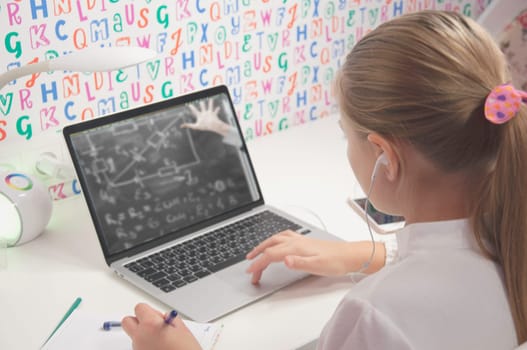 A schoolgirl girl of blond European appearance in headphones is studying online from home, doing her homework. Distance learning teenager on laptop doing homework. Distance learning concept