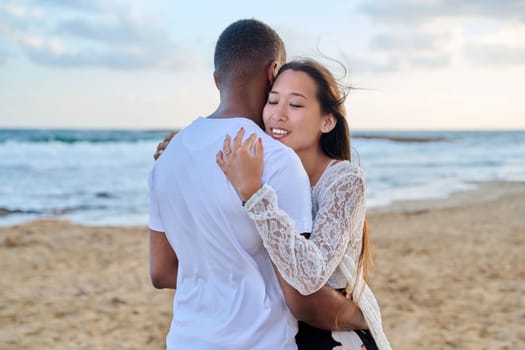 Young loving couple hugging on the beach. Face of beautiful Asian woman, man back. Love, relationship, honeymoon, vacation together, happiness, romantic, travel, family concept