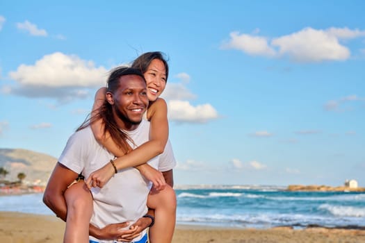 Happy young beautiful couple having fun on beach, copy space. Afro american asian couple laughing enjoying vacation in seaside nature. Multicultural, multiethnic family, relationships, togetherness