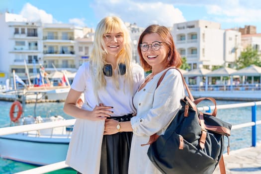 Happy mother and teenage daughter together on the sea promenade. Smiling mom and girl looking at camera, summer vacation, travel tourism, relationship parent teenager, family concept