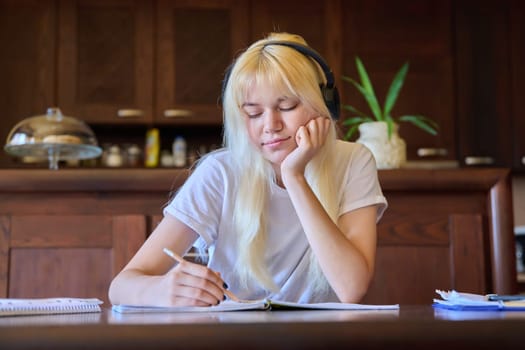 Portrait of a teenage student girl in headphones studying at home, sitting at the table. Technology, high school, college, education, knowledge, e-learning concept