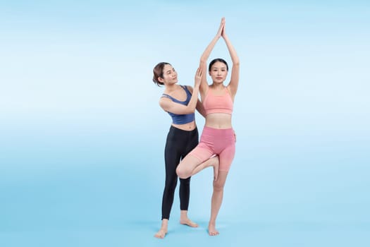 Asian woman in sportswear doing yoga exercise in standing pose with her trainer or yoga buddy. Healthy body care and meditation yoga lifestyle in full shot on isolated background. Vigorous