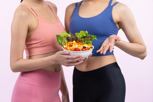 Two young sporty Asian women in sportswear holding salad bowl fill with fruit and vegetable. Natural youthful and fit body lifestyle people with balance nutrition on isolated background. Vigorous