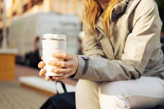 a smiling girl of European appearance with blond hair sits on a bench, looks at the phone and smiles, the girl sits in a gray jacket and white sweatpants. High quality photo