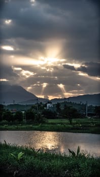 Sun Rays through clouds, sunset above mountains, golden reflection in lake surface water, comfort kindness energy.