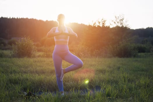 A yoga woman at a serene sunset in the park does a pose for balance and stretching. Meditation and balance exercises at sunrise or sunset with female yoga exercising in nature. High quality photo