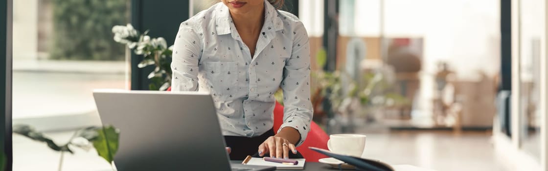 Focused stylish business woman working on laptop sitting the desk on modern office background