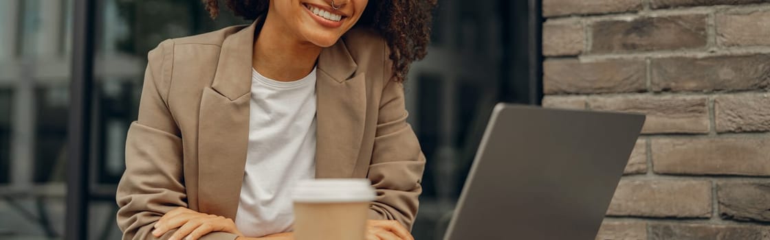 Smiling female freelancer working on laptop while sitting in cafe terrace. Distance work concept