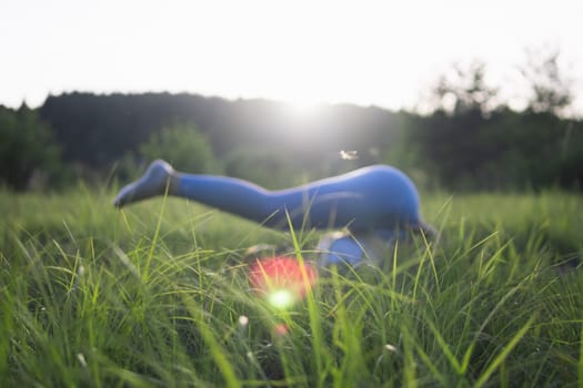 a girl in blue leggings does a stretching throwing her legs over herself lying in a park outdoors. The concept of a healthy body, side view, focus on the grass background blurred. High quality photo