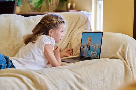 Girl child watching video stream on laptop, resting lying on sofa at home.