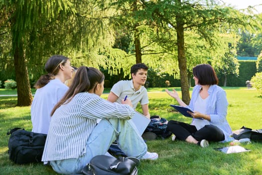 Group of high school students with female teacher, outdoor on campus lawn. Education, college, training, teenagers concept