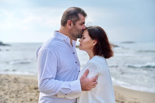 Mature happy loving couple kissing on the sea beach. Wedding, honeymoon, middle aged people relationship, feelings, lifestyle, holidays, dating concept