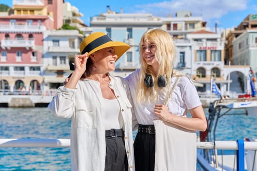 Mother and teenage daughter standing together on sea city embankment, talking laughing. Women tourists resting in summer European tourist town. Family, parent teen relationship, travel, communication