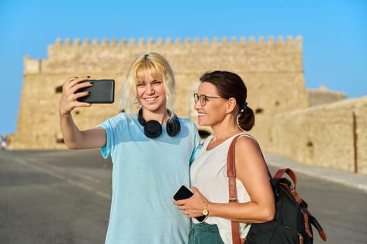 European summer vacation, mom and teenage daughter taking a selfie near the old historic fortress. Family, lifestyle, relationship, travel, tourism concept