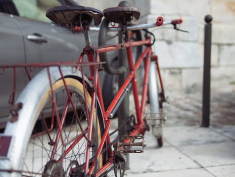 a red bicycle, rare for two people, with two seats, stands in the parking lot next to a gray car. Close-up of a bike from the back. High quality photo